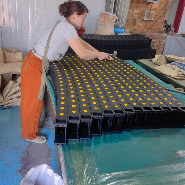 Factory workers manually assembling industrial plastic drag chain links on workbench